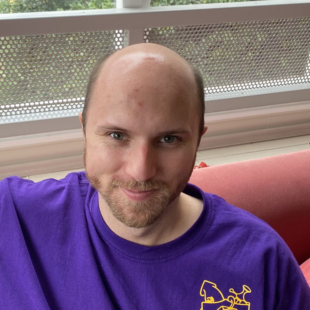 smiling bald man in a purple t-shirt on a red couch