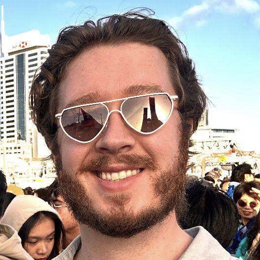 Smiling man in heart shaped mirrored sunglasses, in a crowded outdoor space