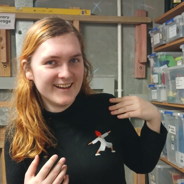 Smiling long haired woman iwth long red hair in a black long sleeved shirt with funky logo